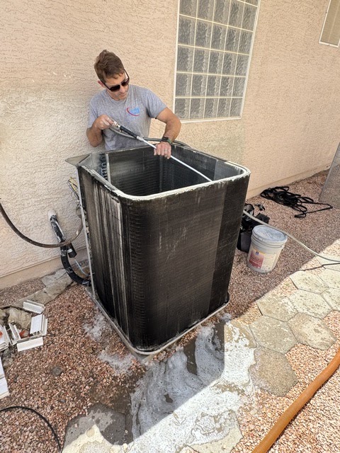 Technician pressure-washing condenser coil fins during tune-up