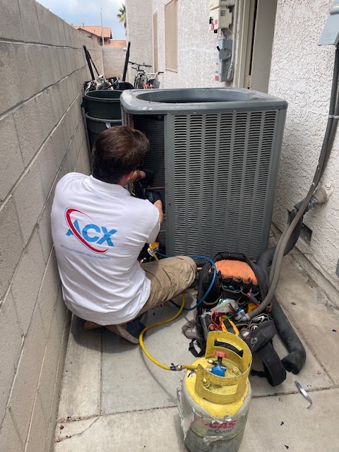 ACX technician servicing condenser with refrigerant gauges and tanks